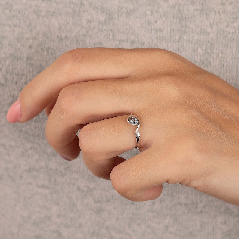 Puede incluir: Un anillo de plata con una piedra preciosa azul claro engastada en una banda curva.