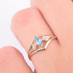 May include: A gold ring with a marquise-shaped blue topaz gemstone and two smaller diamonds. The ring has a delicate, open design.