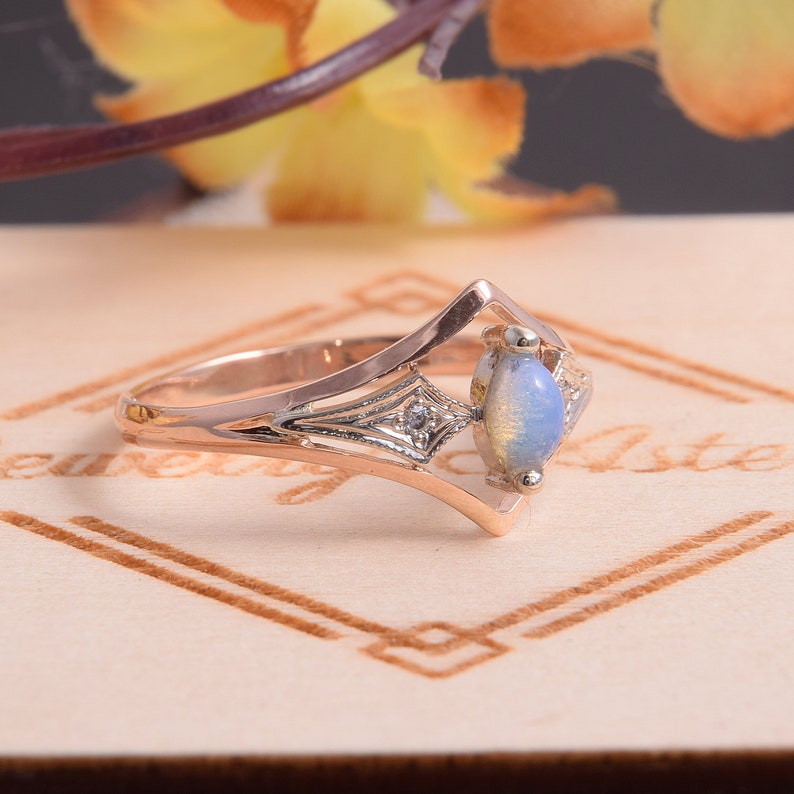 May include: A rose gold ring featuring a marquise-cut opal center stone set in a geometric frame. The band includes intricate silver-toned metalwork with small accent stones embedded in the shoulders, creating a distinct angular profile.