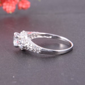 May include: A silver-toned ring featuring a large round-cut clear center stone surrounded by a halo of smaller clear stones. The band is split into two rows, each encrusted with multiple tiny clear stones extending along the sides of the ring.