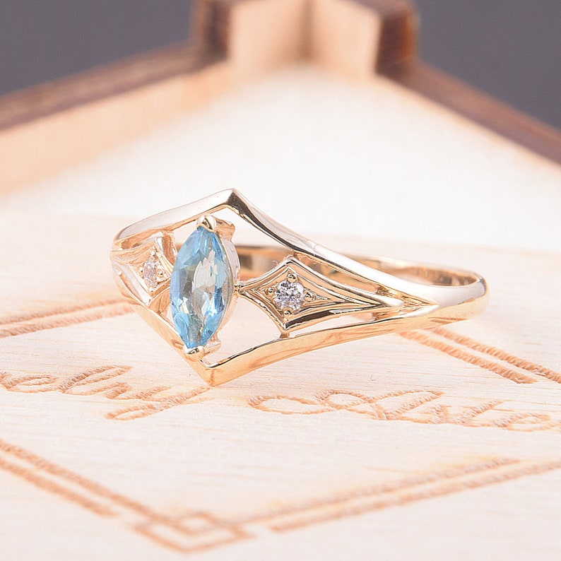 May include: A gold ring with a marquise-shaped blue topaz gemstone and two smaller diamond accents. The ring has a delicate, intricate design.