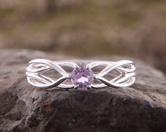 May include: A silver ring with a delicate, interwoven design features a round, light purple gemstone in the centre.