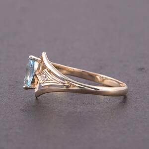 May include: A gold ring with a blue oval-shaped gemstone and a small diamond accent. The ring has a delicate, intricate design.