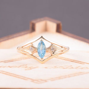 May include: A gold ring with a marquise-shaped blue topaz gemstone surrounded by two smaller diamonds. The ring has a delicate, intricate design.