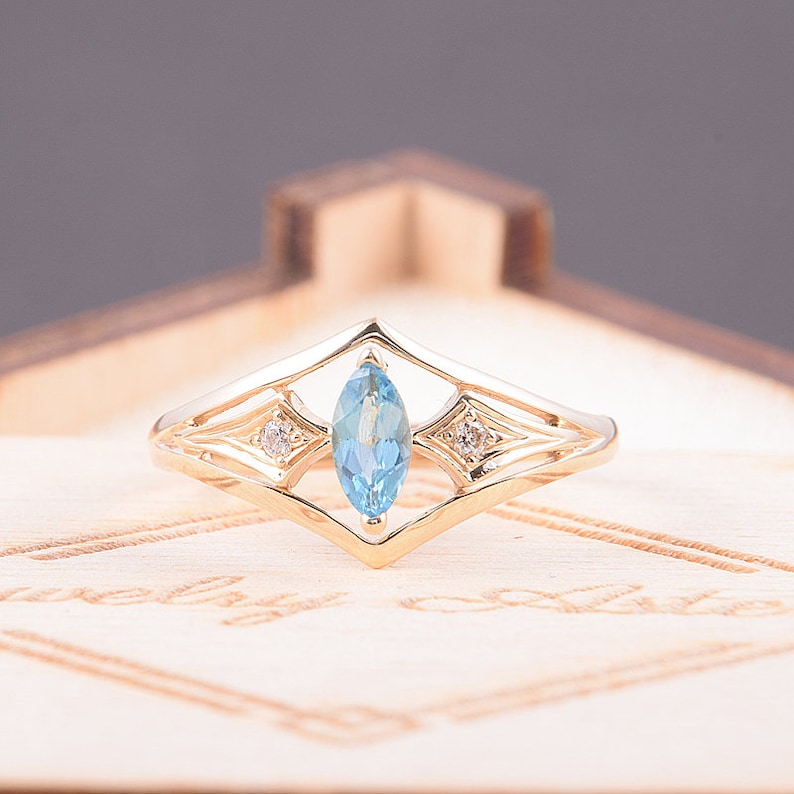 May include: A gold ring with a marquise-shaped blue topaz gemstone surrounded by two smaller diamonds. The ring has a delicate, intricate design.