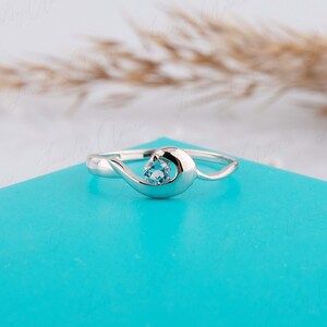 Puede incluir: Un anillo de plata con un dise&ntilde;o de onda delicado y una piedra preciosa azul claro en el centro.