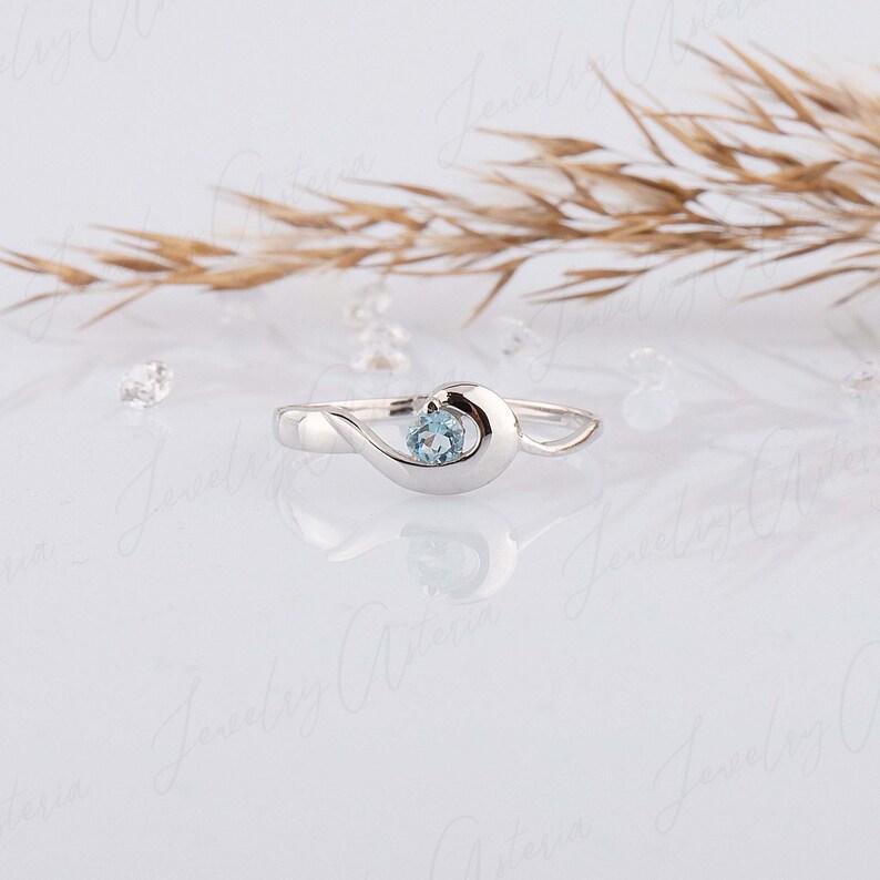 Puede incluir: Un delicado anillo de plata con una piedra preciosa azul claro engastada en un dise&ntilde;o en forma de ola.