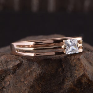 May include: A gold ring with three bands and a single square-shaped clear stone.