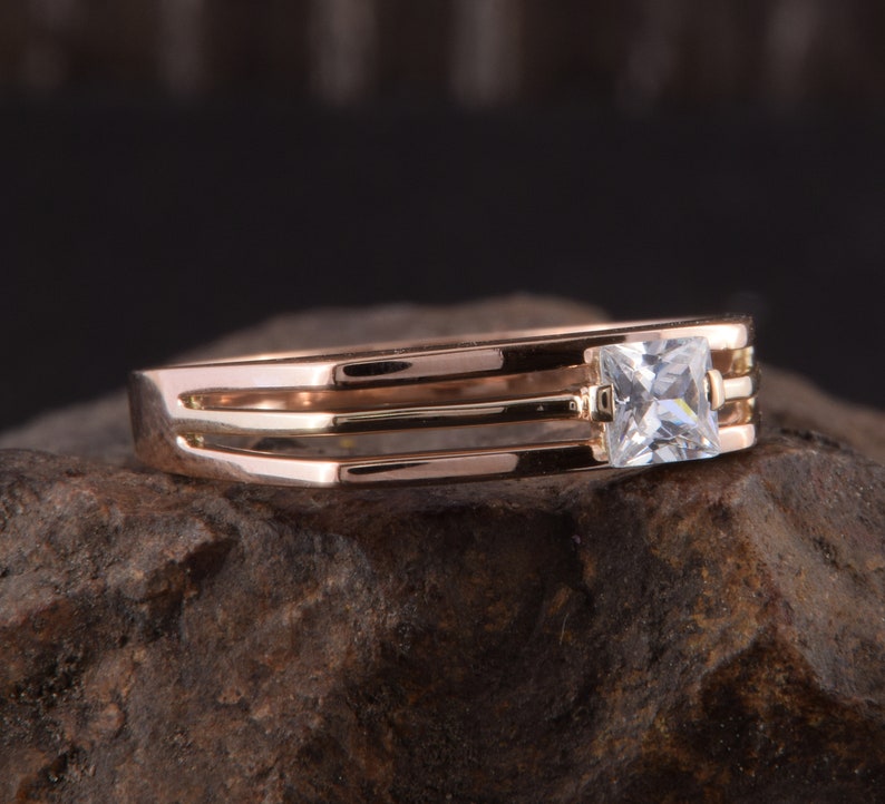 May include: A gold ring with three bands and a single square-shaped clear stone.