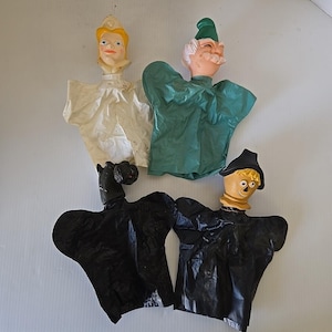 May include: Four vintage hand puppets. One puppet has a blonde head with a white dress. Another has a green hat and green shirt. Two puppets are black. One has a straw-like head and black hat. The puppets are made of plastic and fabric.