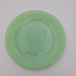 Puede incluir: Un plato redondo verde claro con un borde acanalado. El plato tiene un acabado liso y brillante y un centro ligeramente cóncavo. El color es un verde pastel suave, que recuerda al vidrio de jadeíta. Adecuado para servir alimentos.