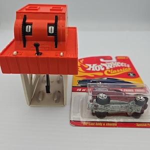 Pode incluir: Um contador mecânico laranja com o número "0" exibido. Um carro de brinquedo Panel Truck vermelho fundido em embalagem plástica. A embalagem tem as palavras "Hot Wheels Classics" e "Special Paint" impressas.