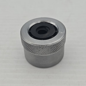 May include: A cylindrical metal object with a textured grip and a black circular insert. The object has a silver finish and a knurled pattern on the lower portion. The top has a smooth, circular design.