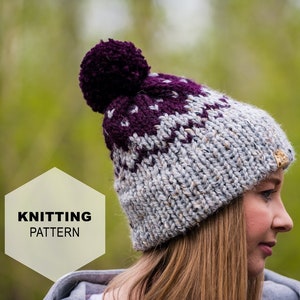 May include: Knitting pattern for a grey and purple beanie with a pom pom on top. The beanie has a white label with the word "KNITTING PATTERN" on it.