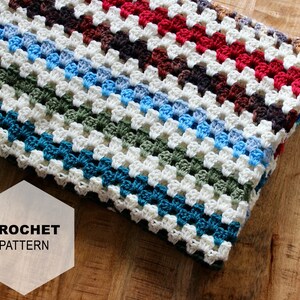 May include: A white crochet blanket with colorful stripes in shades of blue, green, brown, and red. The blanket is folded and lying on a wooden surface. The text "CROCHET PATTERN" is visible in a white hexagon.