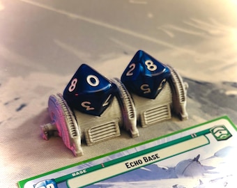 Könnte beinhalten: Zwei blaue Würfel mit weißen Zahlen sitzen auf einer grauen Plastikbasis. Die Basis trägt die Aufschrift "Echo Base". Die Würfel zeigen die Zahlen 2, 8, 0 und 4.