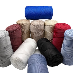 Pode incluir: Uma coleção de 10 rolos de corda colorida, incluindo azul, vermelho, bege, branco, preto e cinza. Os rolos estão dispostos em forma de pirâmide.