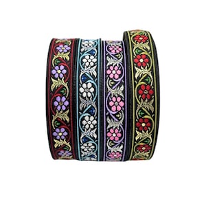 May include: Four rolls of decorative ribbon with floral patterns. The ribbons have a black background with embroidered flowers in purple, white, pink, and red, accented with gold and green leaves. The ribbons are tightly wound.