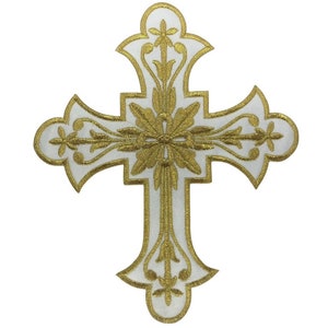 Może przedstawiać: Biały krzyż z haftem złotym. Krzyż ma kwiatowy wz&oacute;r i jest symbolem religijnym.