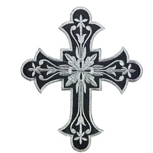 Może przedstawiać: Czarny haftowany krzyż z srebrnymi detalami. Krzyż ma kwiatowy wz&oacute;r i jest symbolem religijnym.