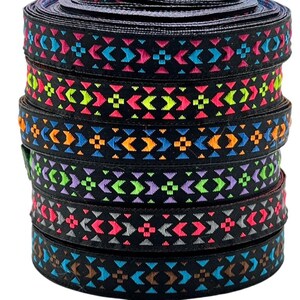 Può includere: Una pila di rotoli di nastro nero con motivi geometrici ricamati colorati. I motivi presentano forme rosa, blu, gialle, arancioni e verdi brillanti. Il nastro è adatto per lavori di artigianato, cucito o scopi decorativi.