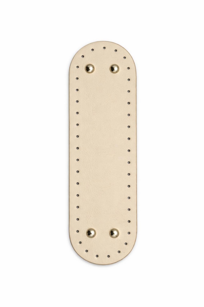 Op de afbeelding: Een langwerpige, ovaalvormige basis van beige leer met afgeronde uiteinden, voorzien van een reeks gelijkmatig verdeelde, voorgeponste gaten langs de gehele rand en vier gepolijste goudkleurige metalen studs bij de boven- en onderkant.
