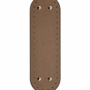Op de afbeelding: Een langwerpige, ovaalvormige beige basis met afgeronde uiteinden, voorzien van een reeks gelijkmatig verdeelde gaatjes langs de gehele omtrek. Twee gepolijste goudkleurige metalen noppen zijn geplaatst nabij de bovenkant en twee onderaan.