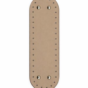 Op de afbeelding: Een langwerpige, ovale beige basis met afgeronde uiteinden, voorzien van een reeks gelijkmatig verdeelde kleine gaatjes langs de gehele omtrek en vier metalen zilverkleurige noppen bij de boven- en onderrand van het oppervlak.