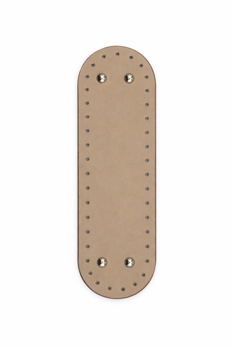 Op de afbeelding: Een langwerpige, ovale beige basis met afgeronde uiteinden, voorzien van een reeks gelijkmatig verdeelde kleine gaatjes langs de gehele omtrek en vier metalen zilverkleurige noppen bij de boven- en onderrand van het oppervlak.