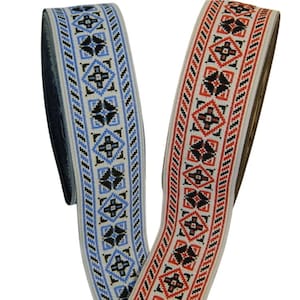 Può includere: Due rotoli di passamaneria in tessuto bianco con motivi geometrici neri, rossi e blu. La passamaneria ha un design intrecciato.