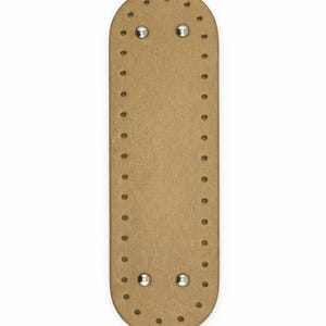 Op de afbeelding: Een langwerpige, ovale, beige basis met afgeronde uiteinden, voorzien van een reeks gelijkmatig verdeelde, voorgeponste gaten langs de gehele omtrek. Vier gepolijste, zilverkleurige metalen klinknagels zijn bevestigd nabij de randen.