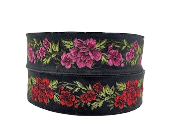 Puede incluir: Cinta negra con ribete de flores bordadas en rosa y rojo. La cinta es de doble capa y tiene un patrón floral.