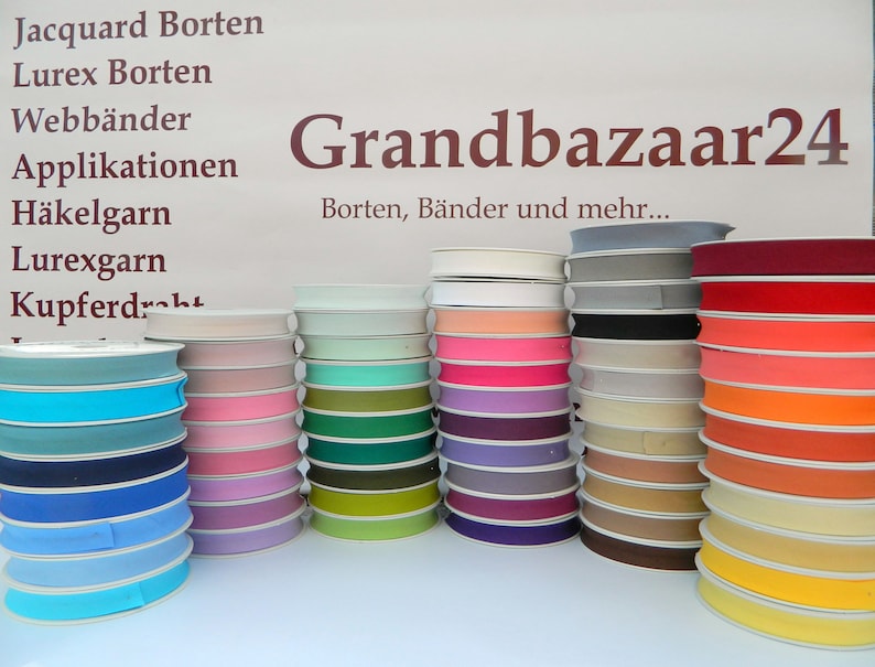 May include: A variety of colors of ribbon spools, including white, pink, teal, green, purple, beige, orange, and yellow. The spools are stacked on a white surface. The text "Grandbazaar24" is visible in the background. Borten, B&auml;nder und mehr... is also visible in the background.