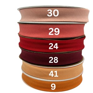 May include: A stack of six rolls of fabric ribbon in various shades of red, orange, and pink. The numbers 30, 29, 24, 28, 41, and 9 are printed on the rolls.