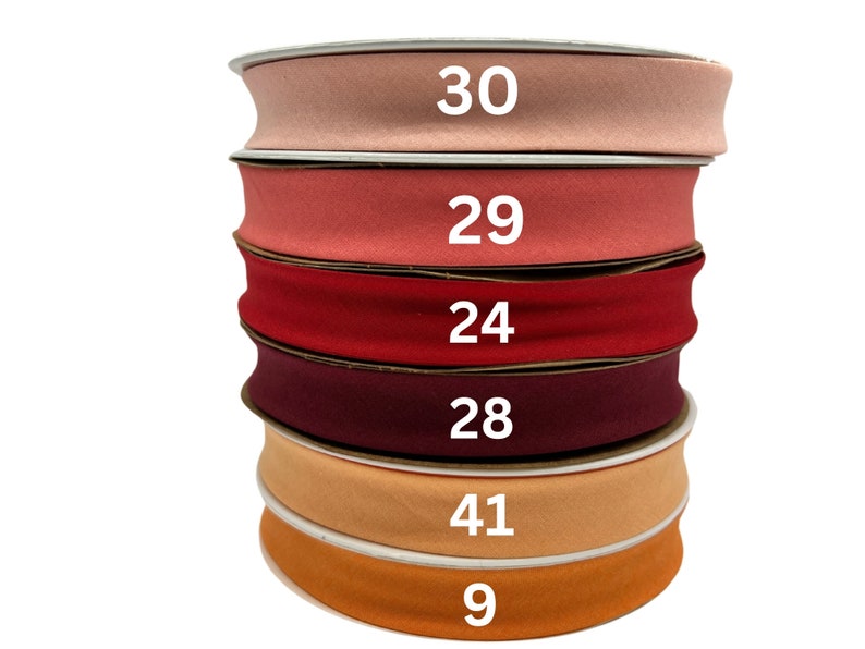 May include: A stack of six rolls of fabric ribbon in various shades of red, orange, and pink. The numbers 30, 29, 24, 28, 41, and 9 are printed on the rolls.