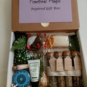 May include: A gift box labeled "Contents of your Practical Magic Inspired Gift Box" filled with various items. Includes a tube of "Morning Mint" lotion, small glass jars with corks, a blue circular item, and a bar of soap.