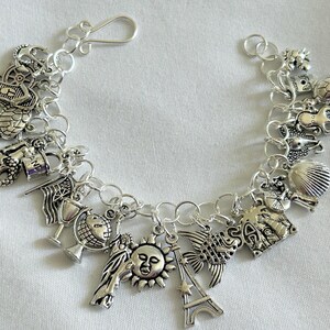 May include: A silver charm bracelet with a variety of charms, including a mermaid, a globe, a sun, a Eiffel Tower, a seashell, a house, and a fish. The charms are attached to a silver chain.