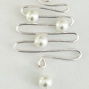 May include: A silver-toned wire earring with a tree-like design. The earring features four faux pearls and a dangling pearl at the bottom. The design is simple and elegant, suitable for everyday wear or special occasions.