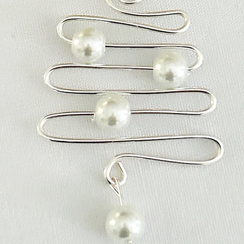 May include: A silver-toned wire earring with a tree-like design. The earring features four faux pearls and a dangling pearl at the bottom. The design is simple and elegant, suitable for everyday wear or special occasions.