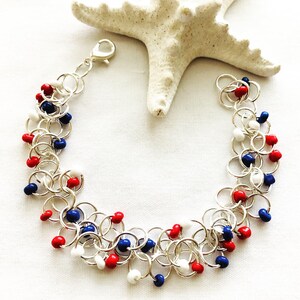 May include: A silver chainmail bracelet with red, white, and blue beads. The bracelet is made of small, interconnected silver rings. The beads are evenly spaced throughout the bracelet, creating a patriotic color scheme.