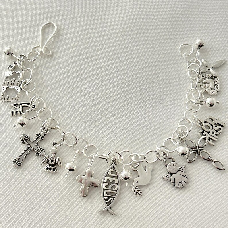 Pu&ograve; includere: Un braccialetto con ciondoli d'argento con simboli religiosi. I ciondoli includono croci, angeli, una colomba e un pesce con la parola "Ges&ugrave;". Il braccialetto &egrave; fatto di catene e ha una chiusura.