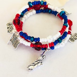 May include: A patriotic bracelet set featuring red, white, and blue beads. The bracelets have charms of the American flag, the Statue of Liberty, and the word "USA". The bracelets are perfect for showing off your American pride.