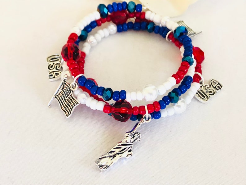 May include: A patriotic bracelet set featuring red, white, and blue beads. The bracelets have charms of the American flag, the Statue of Liberty, and the word "USA". The bracelets are perfect for showing off your American pride.