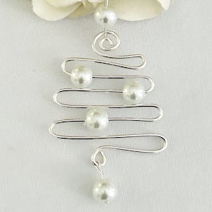 May include: A silver-toned wire Christmas tree ornament with five white pearl accents. The ornament has a spiral at the top and a pearl dangling at the bottom. The background is a soft white fabric.