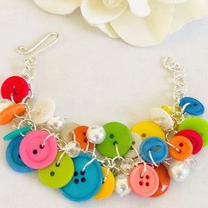 May include: A colorful button bracelet with a silver chain and white pearl accents. The buttons are in various colors, including red, orange, yellow, green, blue, and pink.