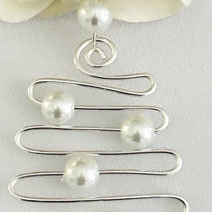 May include: A silver-toned wire Christmas tree ornament with faux pearl accents. The ornament features a spiral at the top and horizontal lines with pearls, creating a festive and elegant design. The background is a soft white.