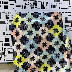May include: A quilt with a patchwork design featuring a variety of colors, including black, white, yellow, and blue. The quilt is made up of small squares and rectangles, and it features a star pattern.