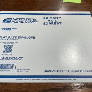 May include: A white USPS Priority Mail Express flat rate envelope. The envelope features the USPS logo, the text "Priority Mail Express", and a barcode. Dimensions are 12 1/2 x 9 1/2 inches.