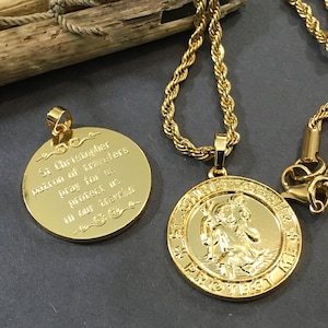 Op de afbeelding: Gouden ketting met een ronde hanger met een afbeelding van Sint Christoffel. De hanger heeft de inscriptie "St Christopher patron of travelers pray for us protect us in our travels".