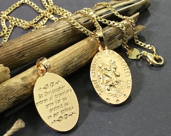 May include: Gold chain necklace with a gold oval pendant featuring a religious image of Saint Christopher. The back of the pendant has an inscription that reads "St Christopher patron of travelers pray for us in our travels".